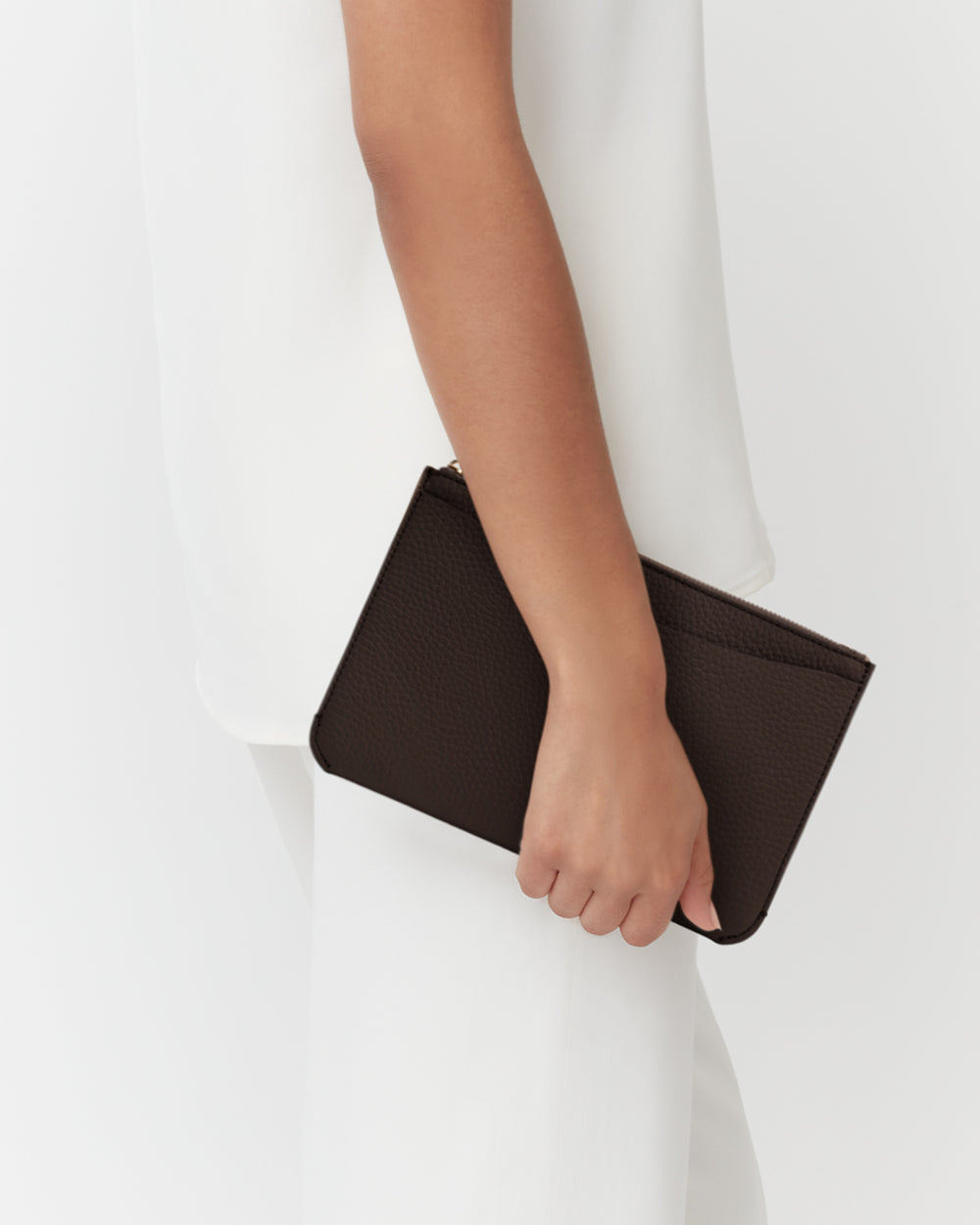 Person holding a small textured clutch against a plain outfit.