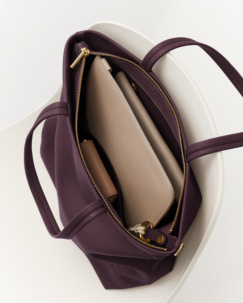 Open tote bag with a laptop and a pouch inside, placed on a chair.