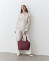 Person in striped shirt and wide pants holding a handbag, standing against a wall.