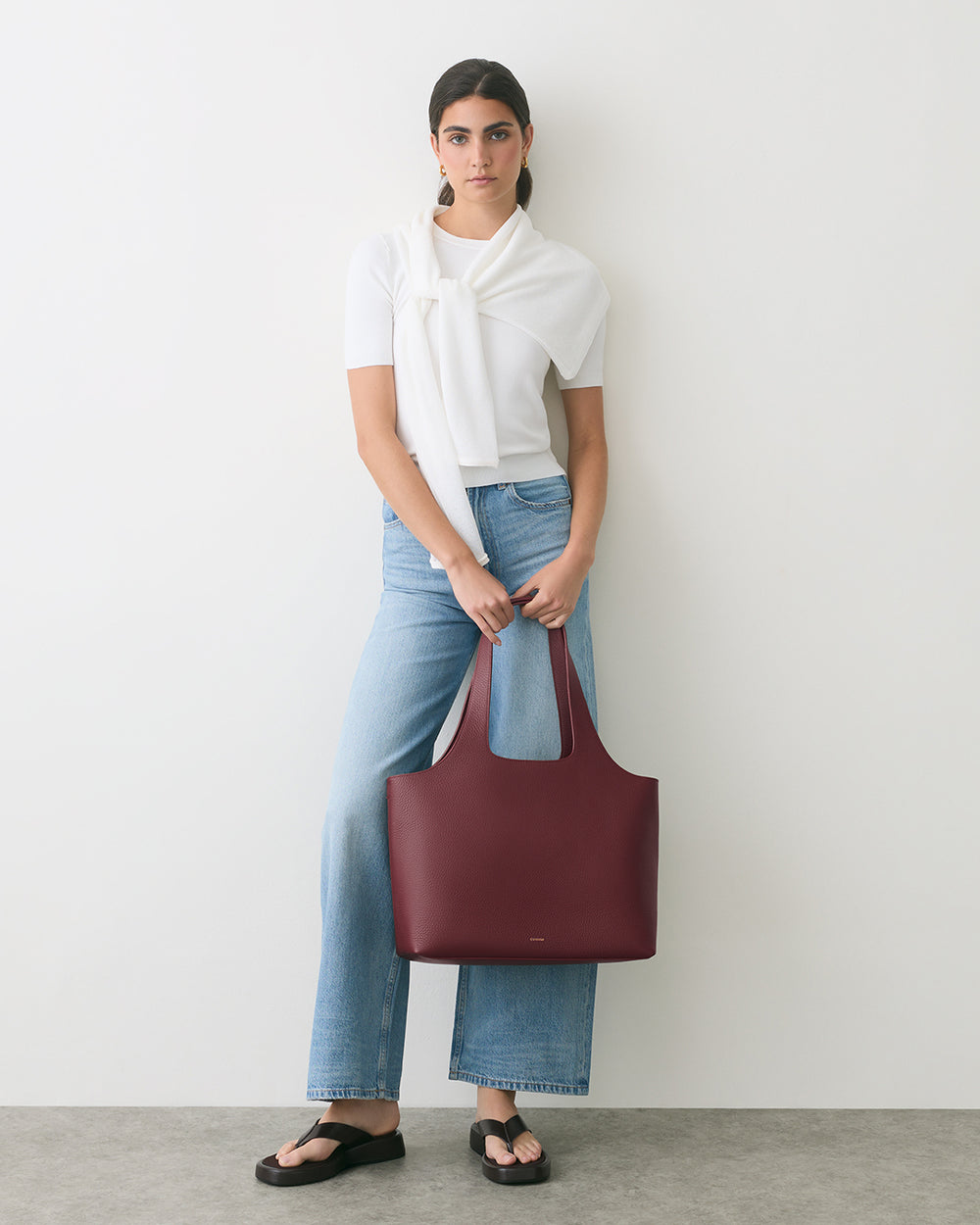 Person wearing jeans, a top, and sandals, holding a large handbag.
