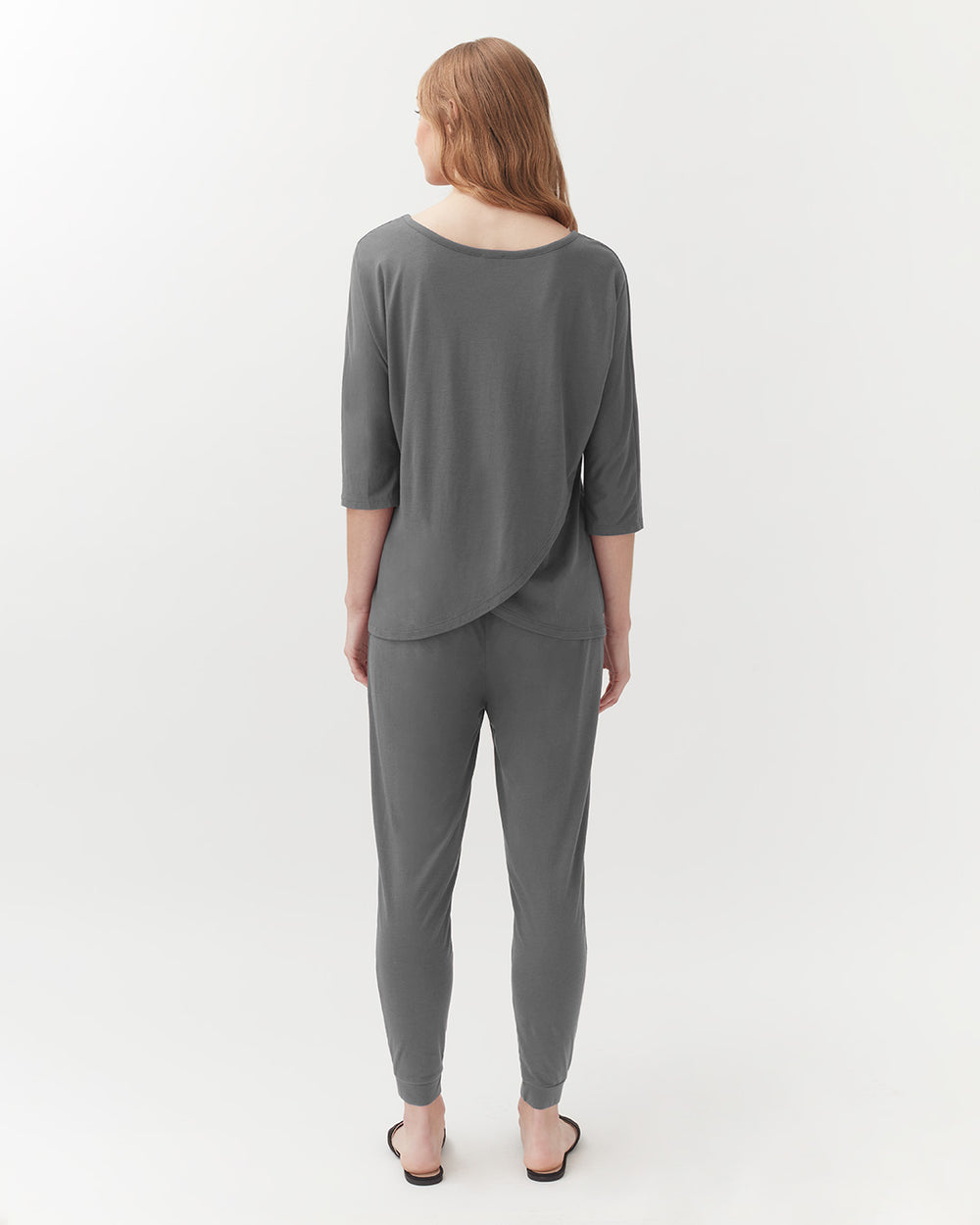 Woman standing facing away, wearing a top and trousers, in a studio setting.