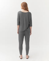 Woman standing facing away, wearing a top and trousers, in a studio setting.