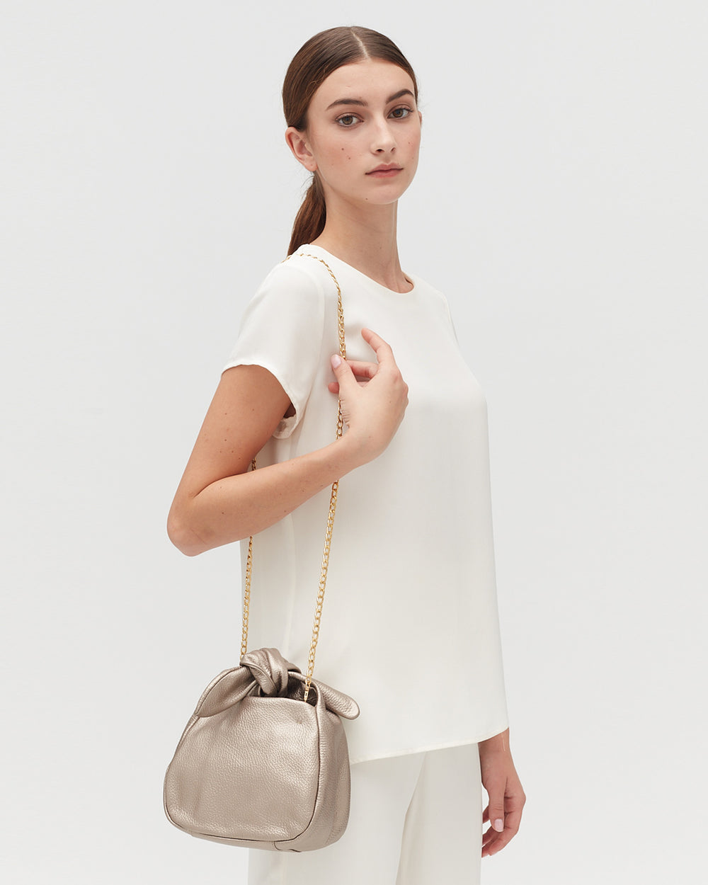 Woman standing and holding a purse with shoulder strap.