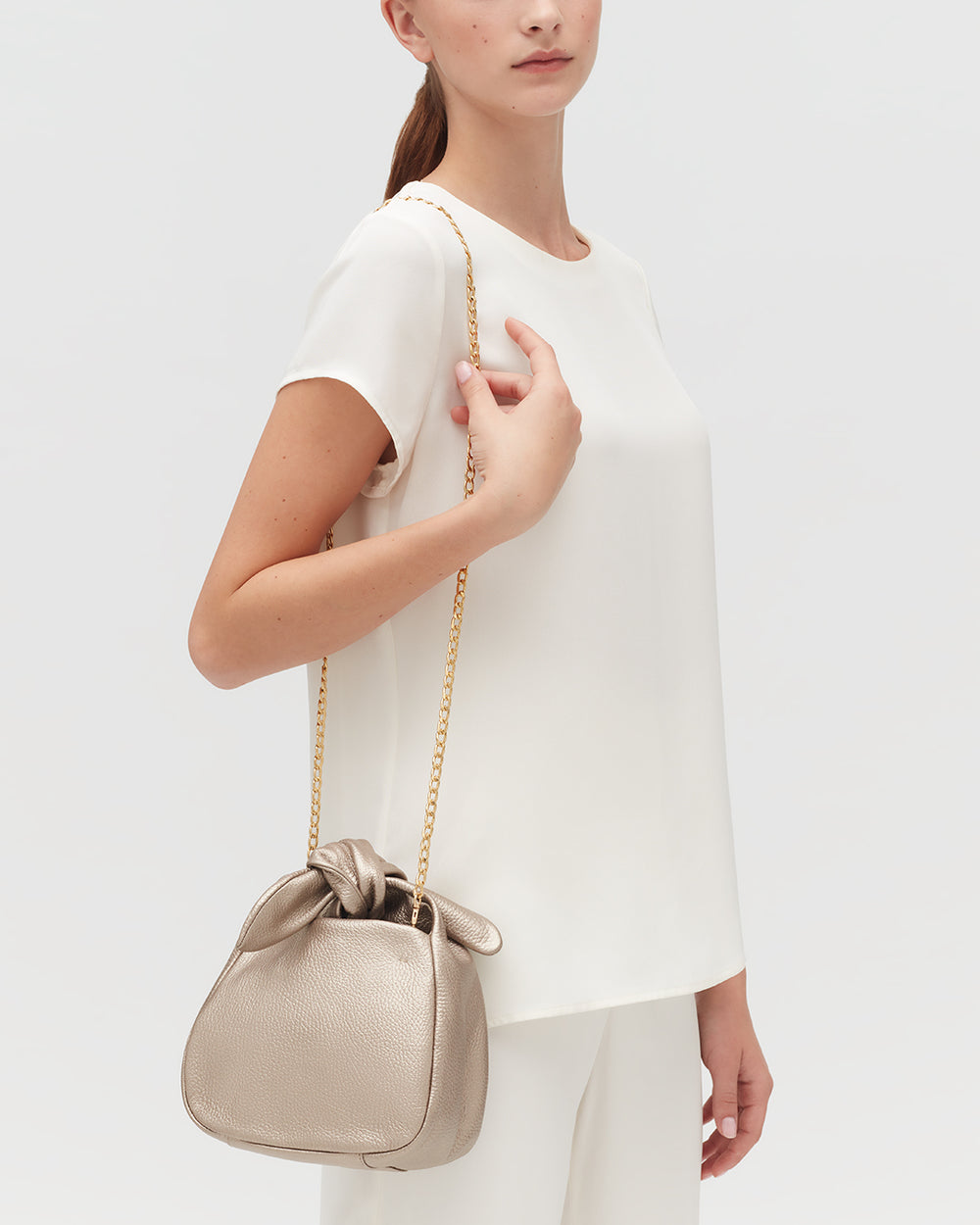 Person in white outfit holding a handbag with a chain strap