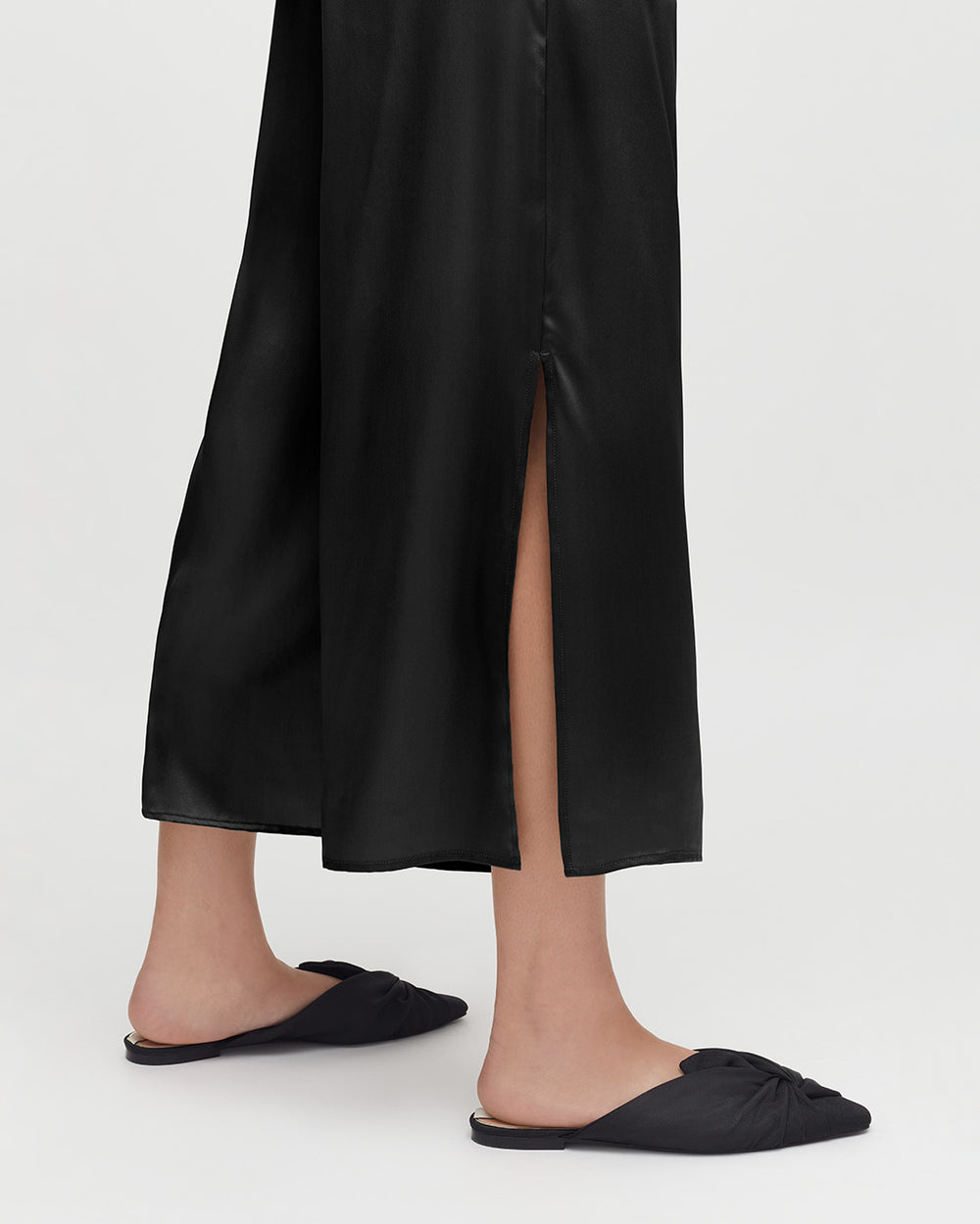 Person wearing long skirt and flat shoes, standing with a visible leg through a skirt slit.