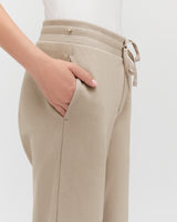 Close-up of a person's hand resting on their hip, wearing high-waisted pants with a tie.