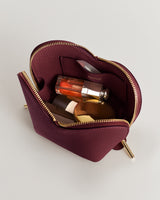 Small open pouch with a zipper, containing lipstick, compact, and perfume bottle.