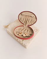 Oval jewelry case with open lid on textured surface.