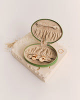 Oval jewelry case with open lid on textured surface.