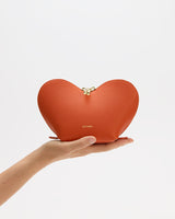 A hand holding a heart-shaped clutch bag with a zipper closure.