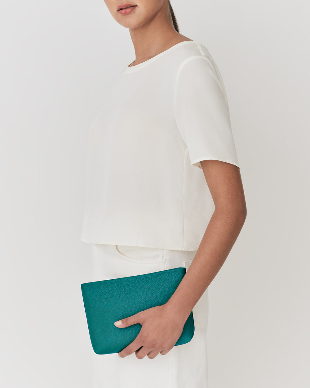 Person holding a clutch bag while wearing a short-sleeve top and pants.