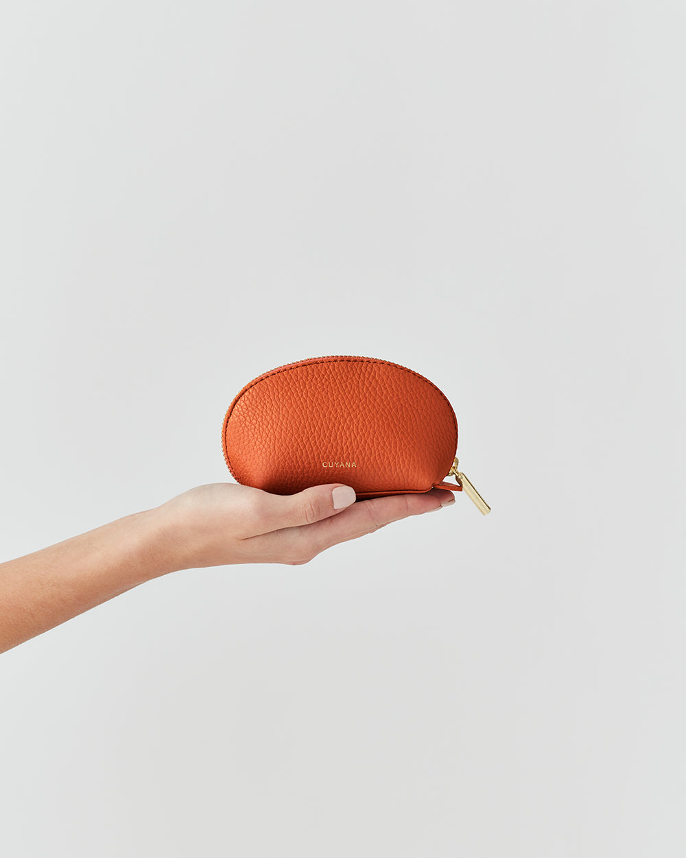 Hand holding a small pouch against plain background.