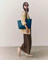 Person wearing a long coat and pants, holding a large shoulder bag.