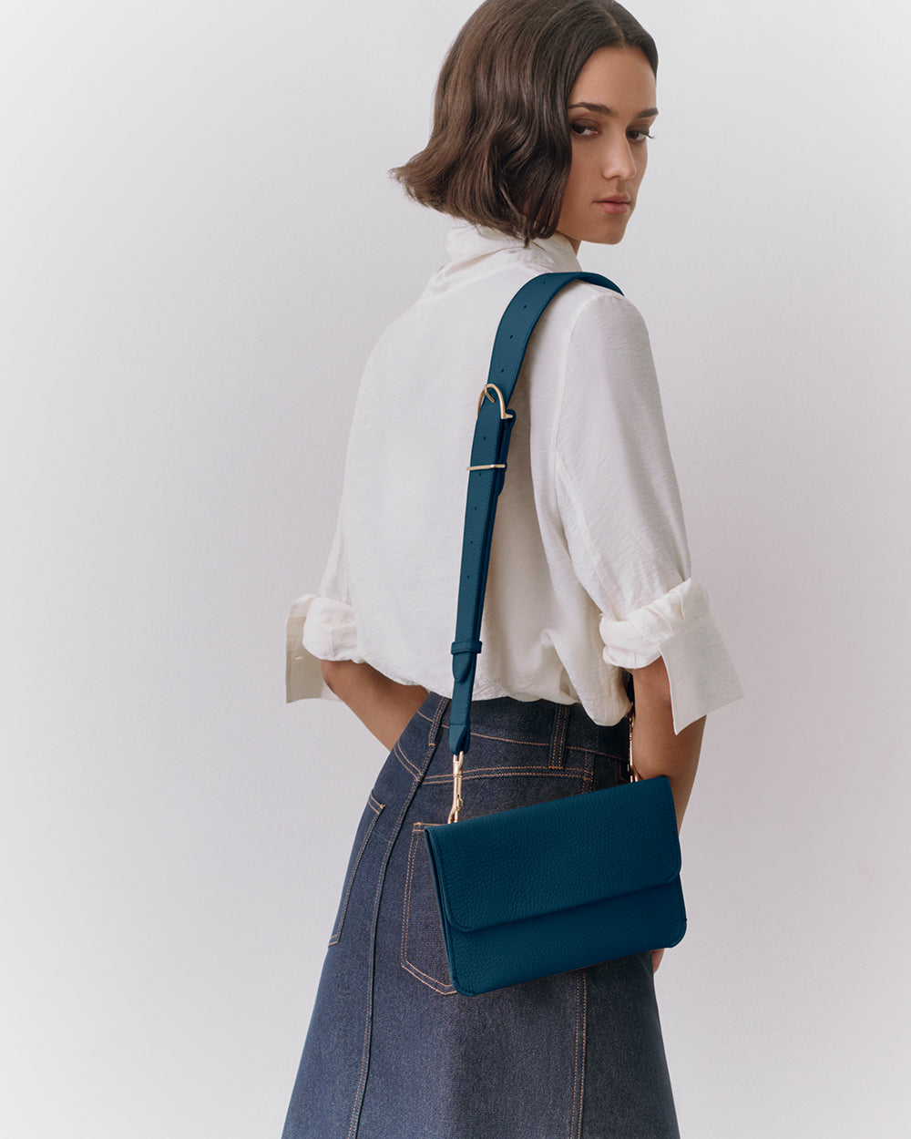 Woman with crossbody purse wearing a shirt and skirt, facing away.