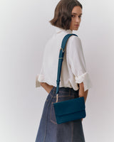 Woman with crossbody purse wearing a shirt and skirt, facing away.