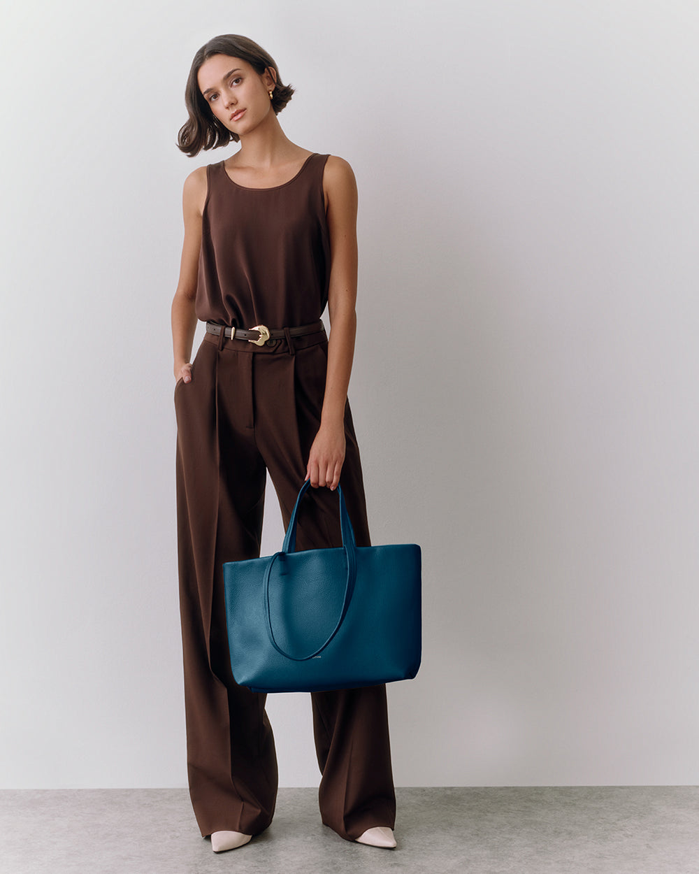 Person in outfit holding tote bag standing against plain background.