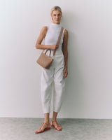 Person standing with a top, pants, sandals, and a small shoulder bag.