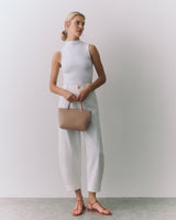 Person in sleeveless top and pants holding a small handbag, wearing sandals.