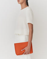 Person holding a clutch under their arm, wearing a short-sleeve top and skirt.