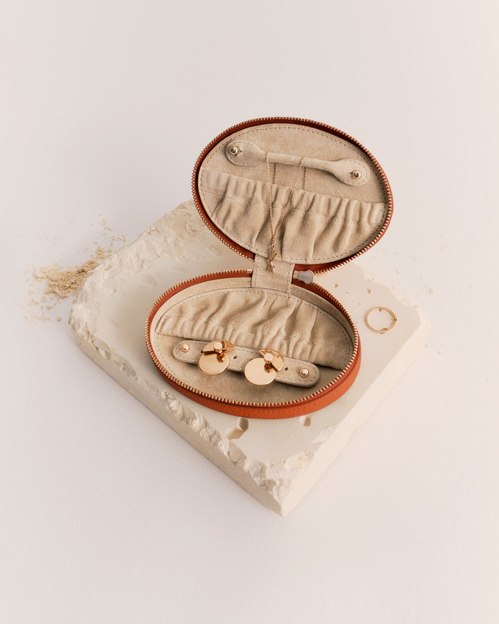 Oval jewelry case open on textured surface with rings scattered nearby.