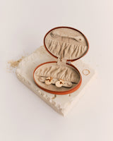 Oval jewelry case open on textured surface with rings scattered nearby.