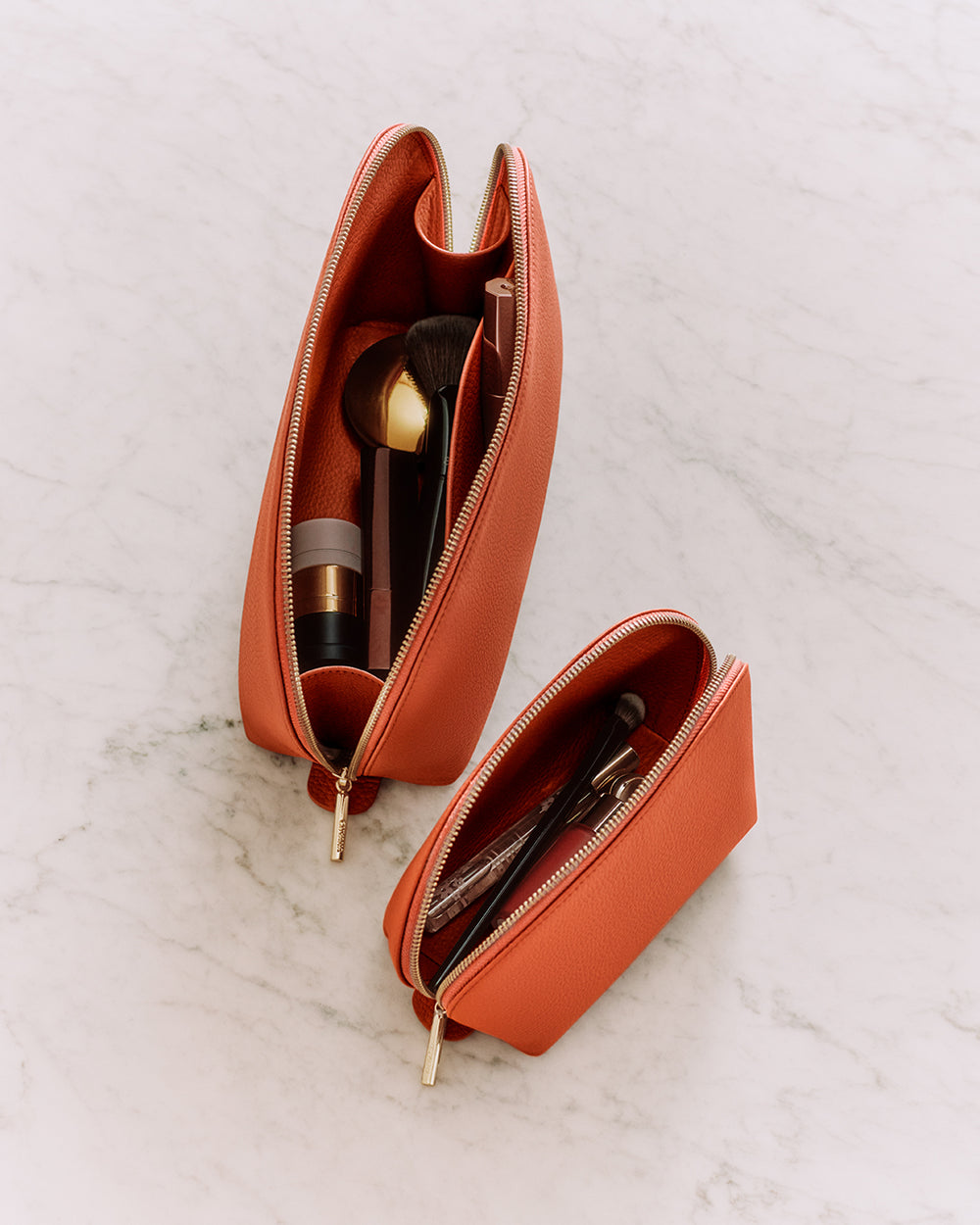 Two zippered pouches with makeup items on a marble surface.