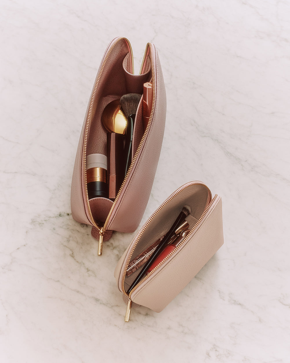 Two makeup bags with brushes and cosmetics inside, placed on a marble surface.