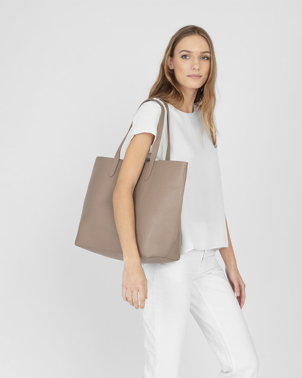 Woman standing with a large tote bag, looking at the camera.