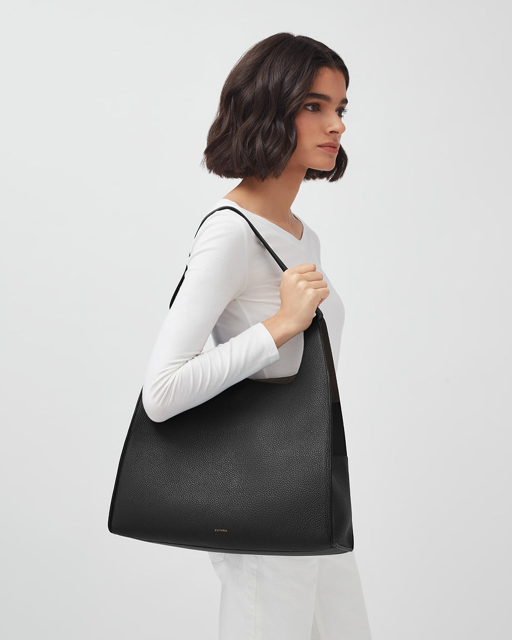 Woman standing sideways holding a large shoulder bag.
