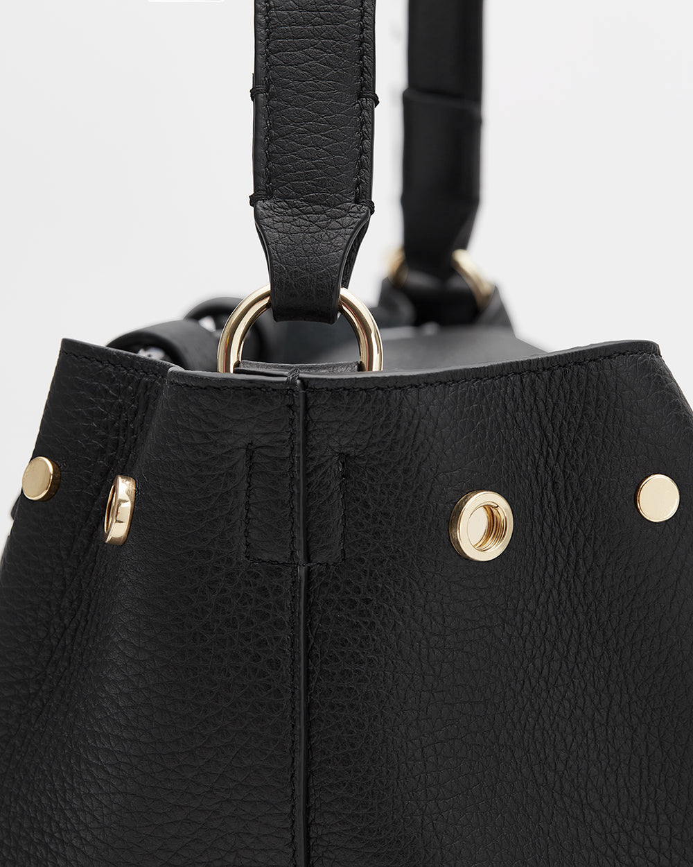 Close-up of a handbag with metallic rivets and a partial view of the handle.