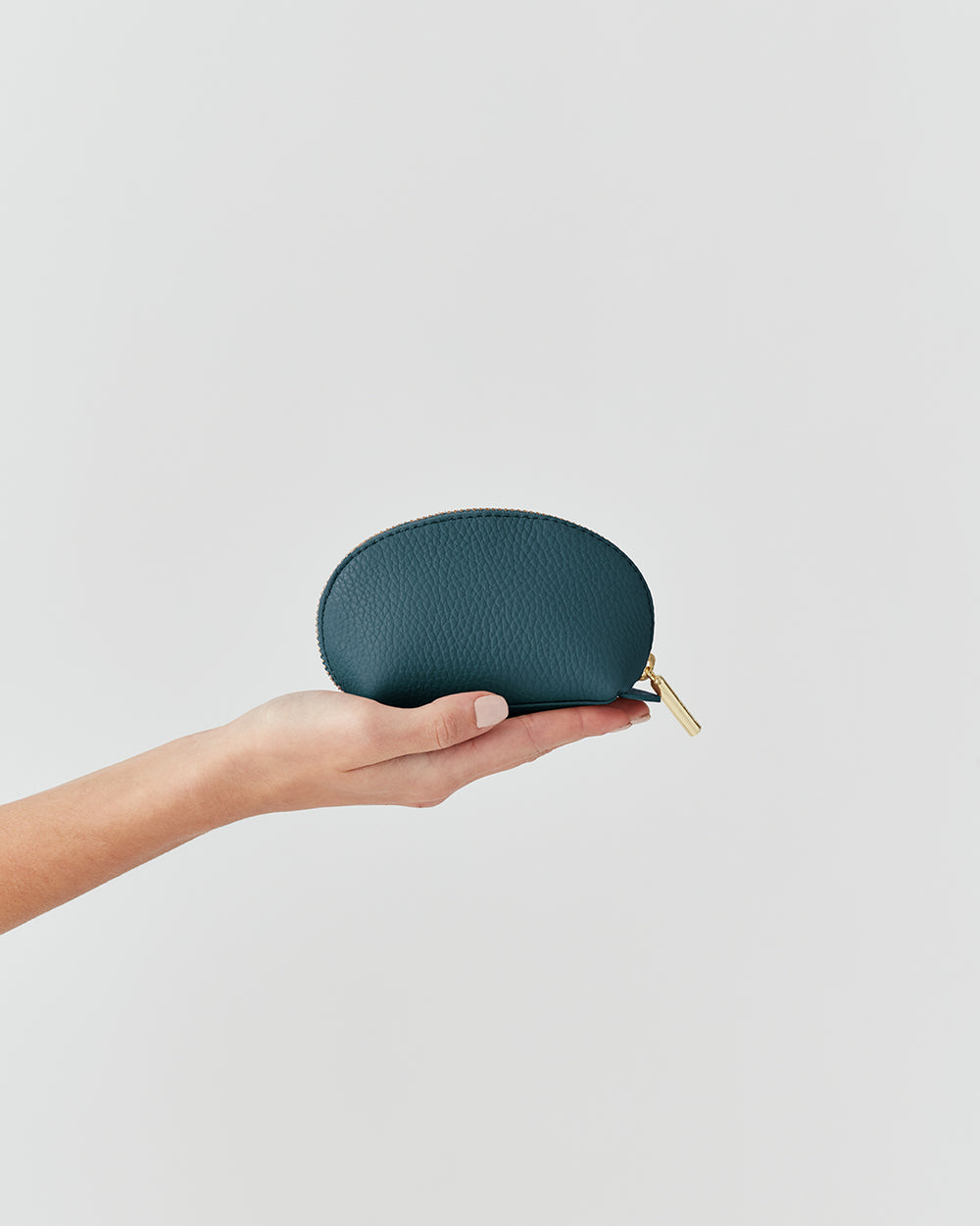 Hand holding a small zippered case against a plain background.