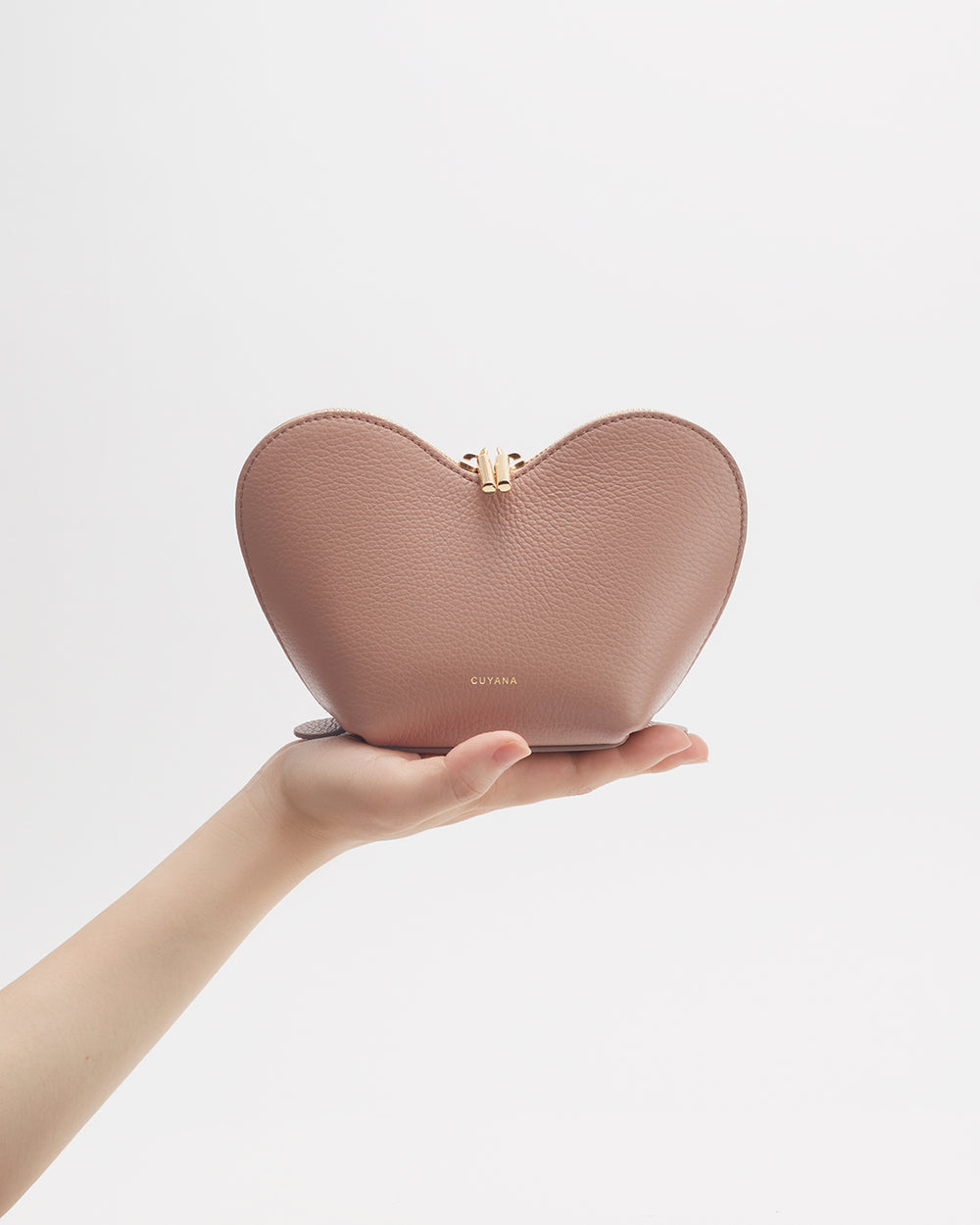 Hand holding a heart-shaped purse against a plain background.