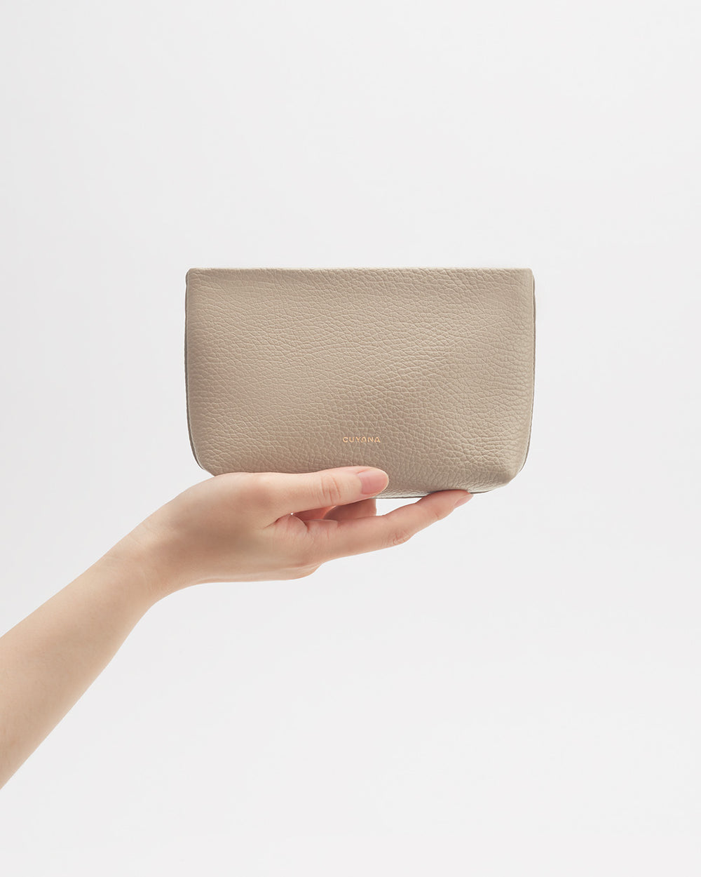 Hand holding a small pouch against a plain background.