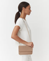 Woman standing sideways with a shoulder bag and ponytail.
