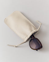 Sunglasses partially in a drawstring case on a plain surface