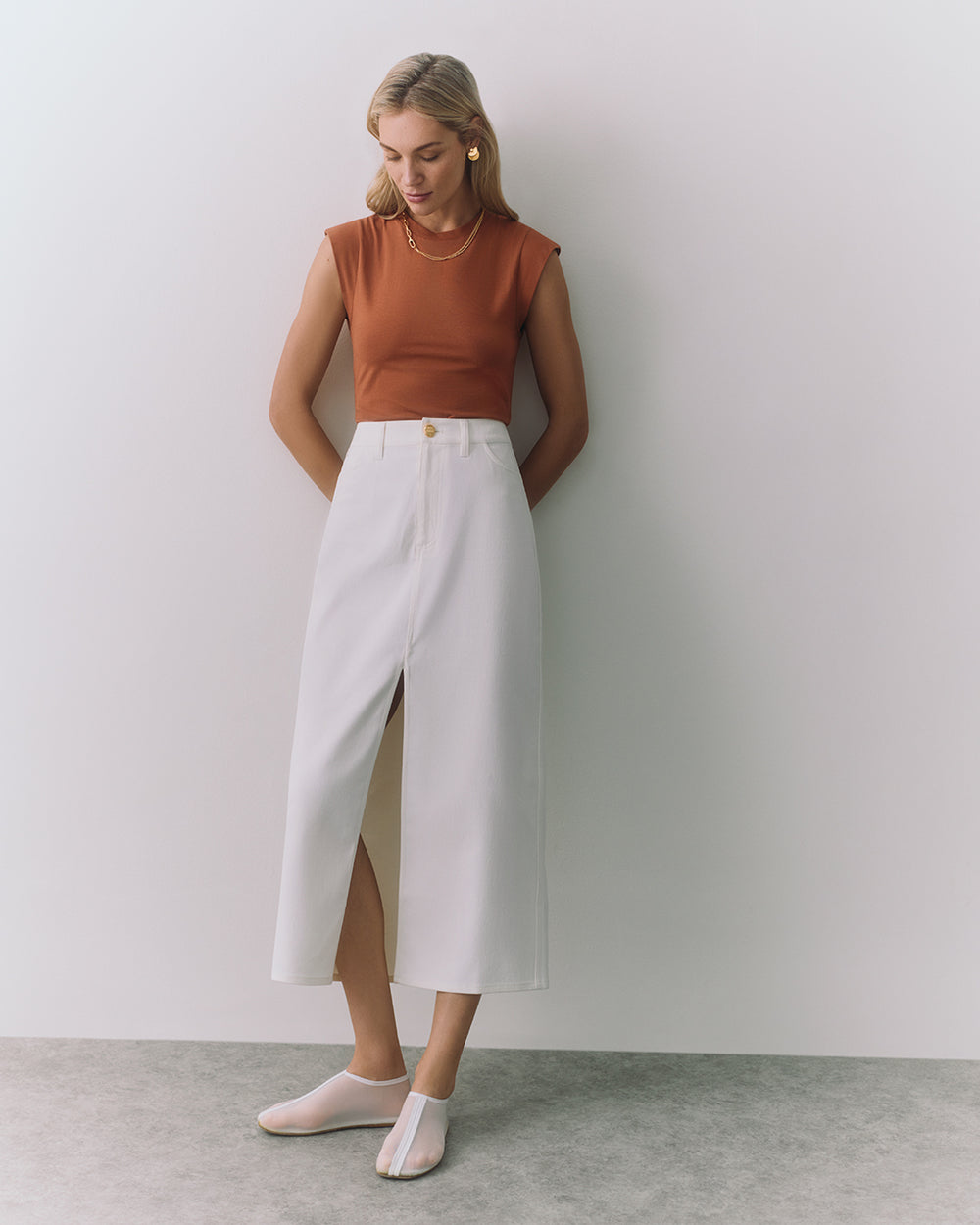 Person wearing sleeveless top and long skirt, standing against the wall.