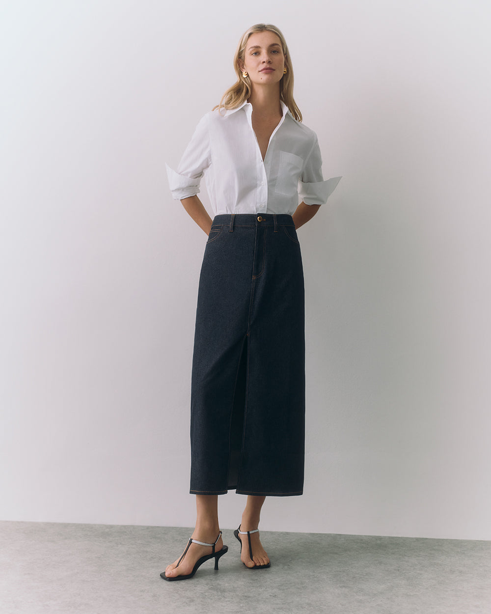 Person wearing a button-down shirt, long skirt, and heels stands indoors.