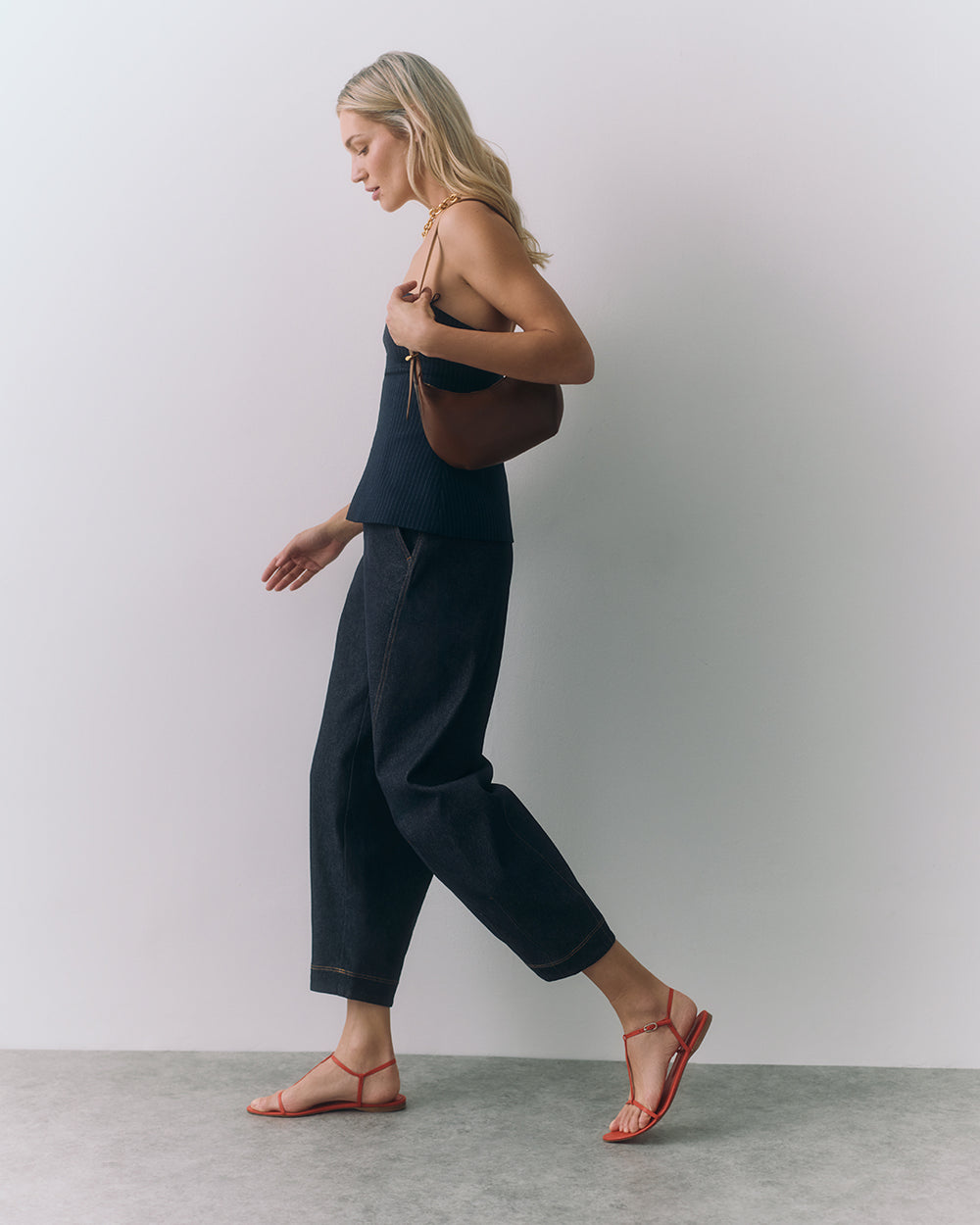 Person walking with a shoulder bag, wearing a sleeveless top and pants, in strappy sandals.