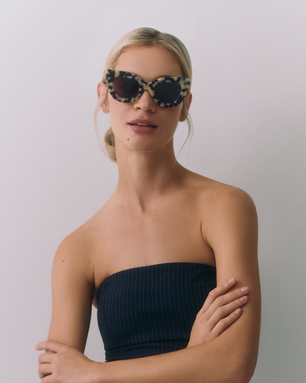 Woman wearing sunglasses and a strapless top, arms crossed.