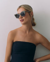 Person wearing sunglasses and strapless top standing against a plain background