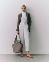 Person in blazer and pants holding a tote bag and wearing sandals.