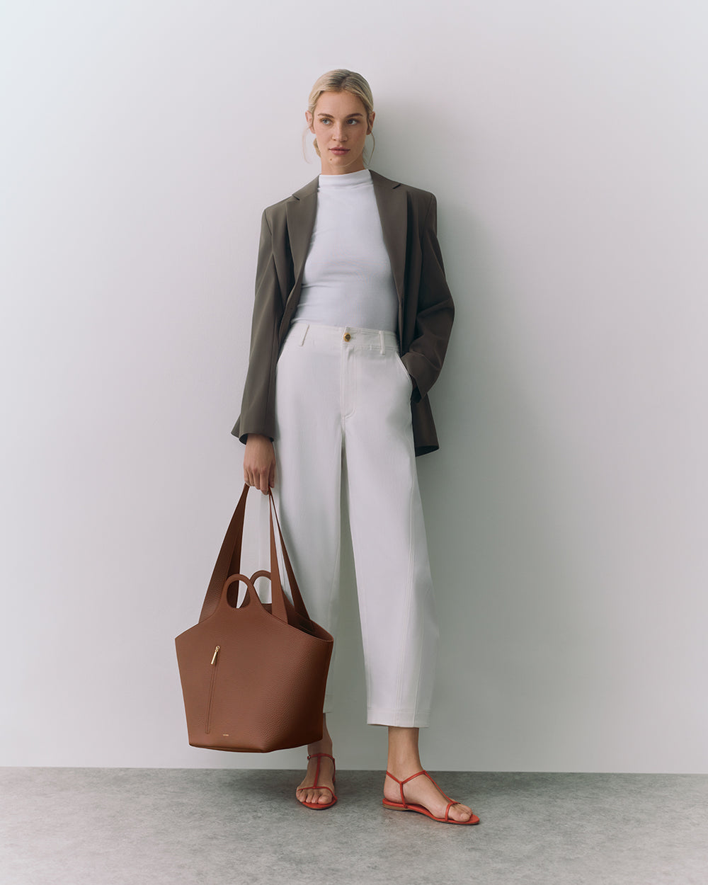 Person standing with a large handbag, wearing a blazer, top, and pants.