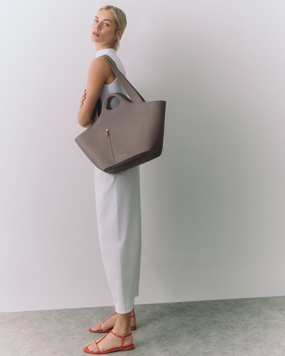 Person in a sleeveless dress carrying a large handbag, standing in a bright space.