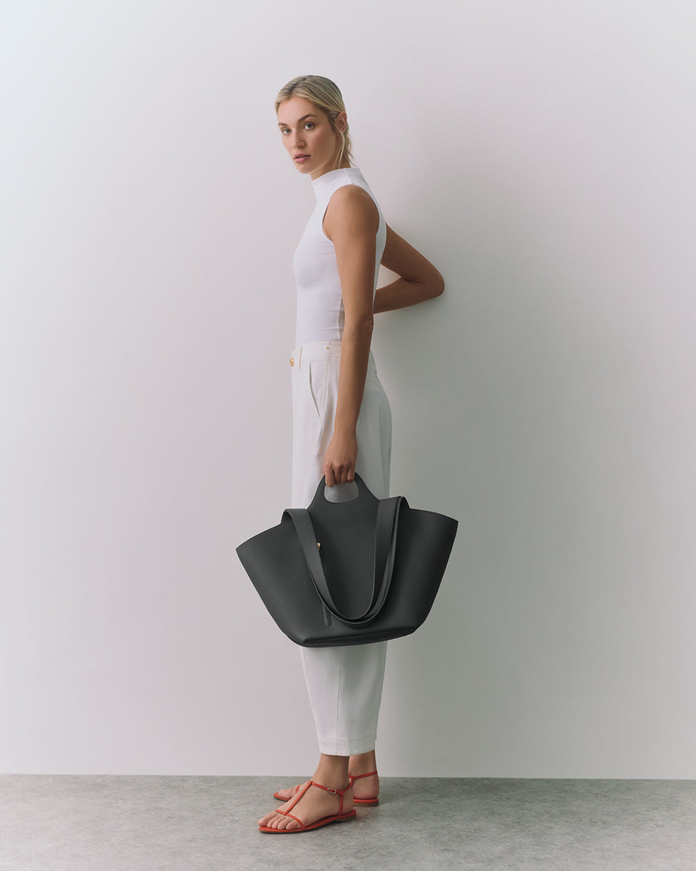 Person standing against wall holding large handbag