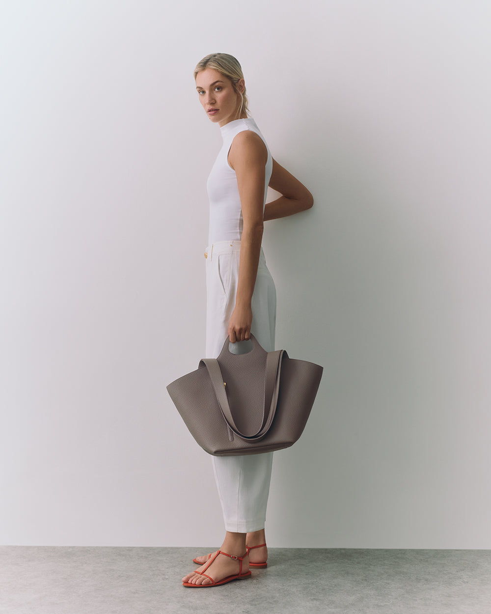 Person standing with a large handbag, wearing sleeveless top and pants, looking at the camera.