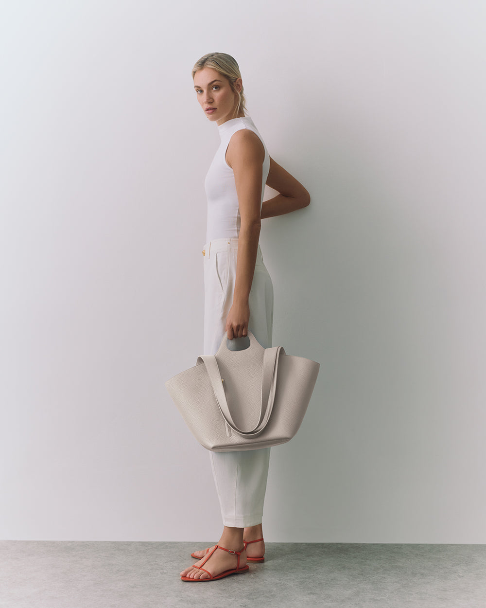 Person holding a large handbag, wearing sleeveless top and pants with sandals.