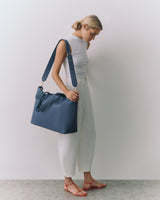 Person standing with a travel bag over their shoulder wearing a sleeveless top and pants.