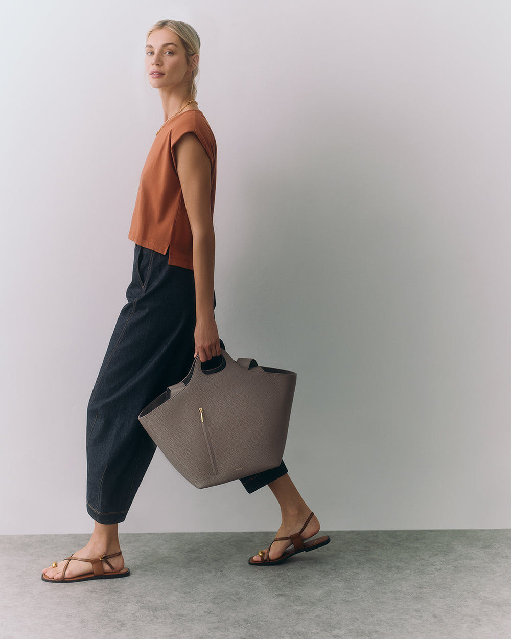 Person walking with sandals, holding a large handbag, wearing a top and loose pants.