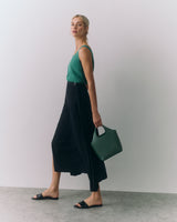 Person in sleeveless top and long skirt holding a handbag, wearing sandals.