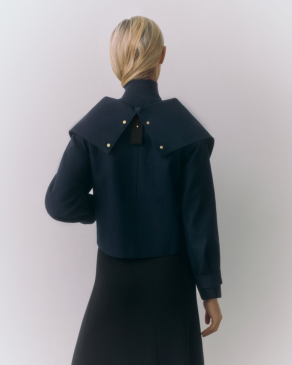 Person wearing a jacket with a cape-like collar, seen from the back.